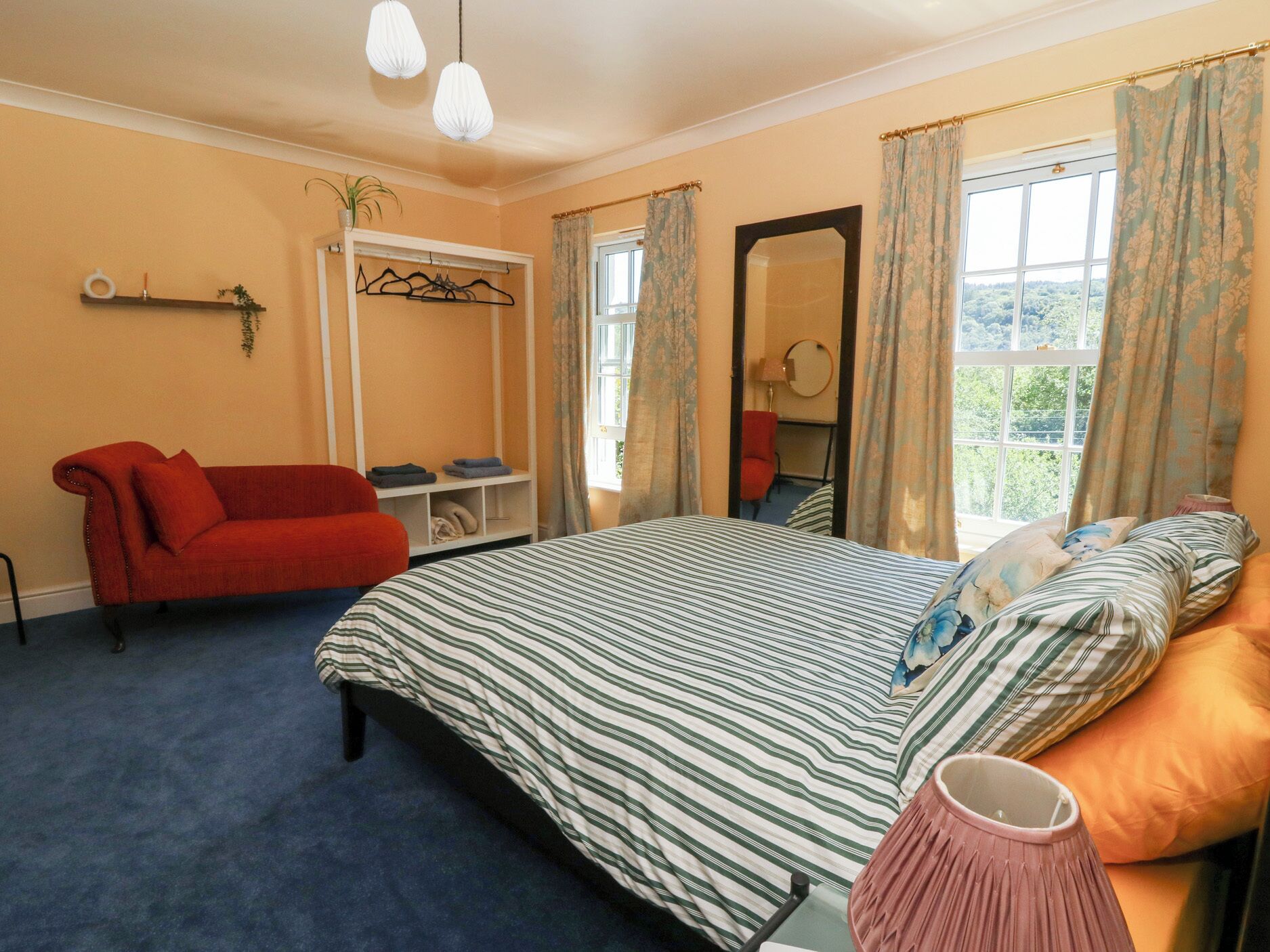 A bedroom with a bed, a red sofa, a mirror, and a window with curtains.