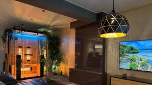 Una sala de estar moderna con un sofá de cuero, un televisor grande y una lámpara colgante de diseño geométrico.
