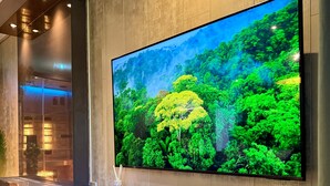 Una sala de estar moderna con un televisor de pantalla plana grande montado en una pared de madera, una consola oscura y una vela decorativa.