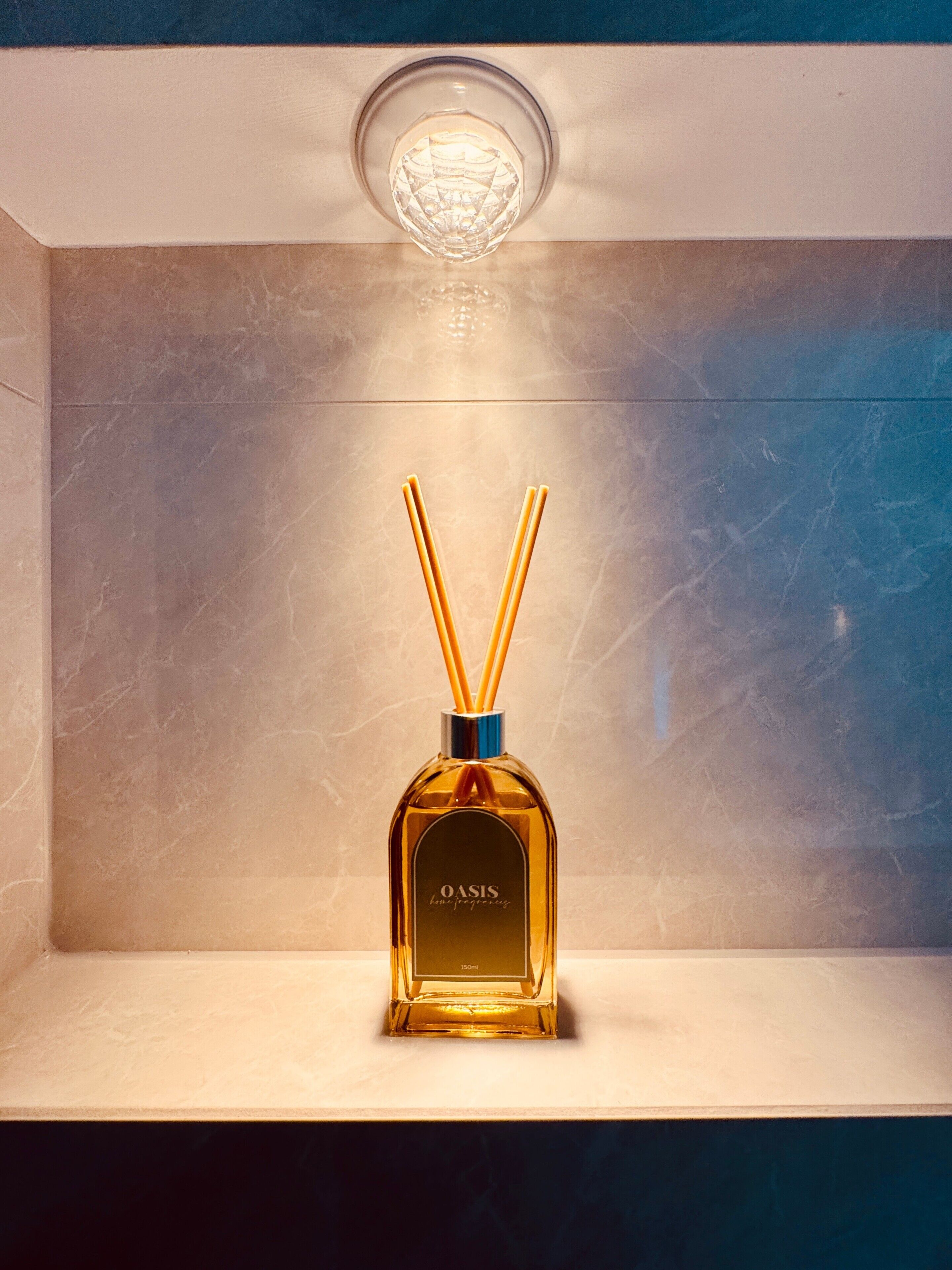 A bottle of OASIS cologne on a shelf with a marble background and a light fixture above.