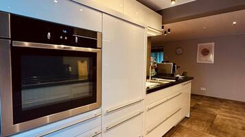 Una cocina moderna con horno empotrado, armarios blancos y suelo de baldosas.