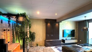 Una sala de estar moderna con un televisor de pantalla plana grande, un sofá de cuero oscuro y un mueble de entretenimiento de madera.