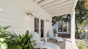 A covered porch with white chairs, a wooden deck, and potted plants.