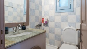 A bathroom with a sink, mirror, toilet, and a shelf with toiletries. - Apartment '7' with sea view, Wi-Fi and air conditioning (Tinos)