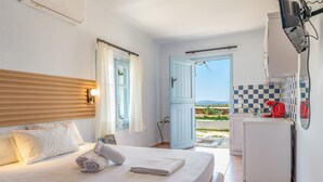 A hotel room with a bed, a small kitchenette, a window with curtains, and a view of the outdoors. - Apartment '7' with sea view, Wi-Fi and air conditioning (Tinos)