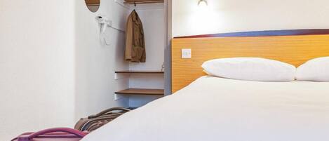 A hotel room with a bed, a coat rack, a suitcase, and a mirror.