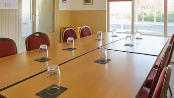 Uma sala de conferências com uma mesa comprida, cadeiras vermelhas e copos de vidro sobre bases.
