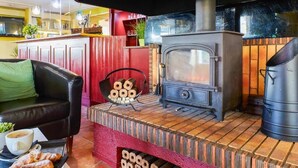A cozy room with a wooden stove, a leather sofa, and a dining table with pastries. - The Kiln Hotel, Wakefield (West Yorkshire), Part of the AG Collection (Wakefield)