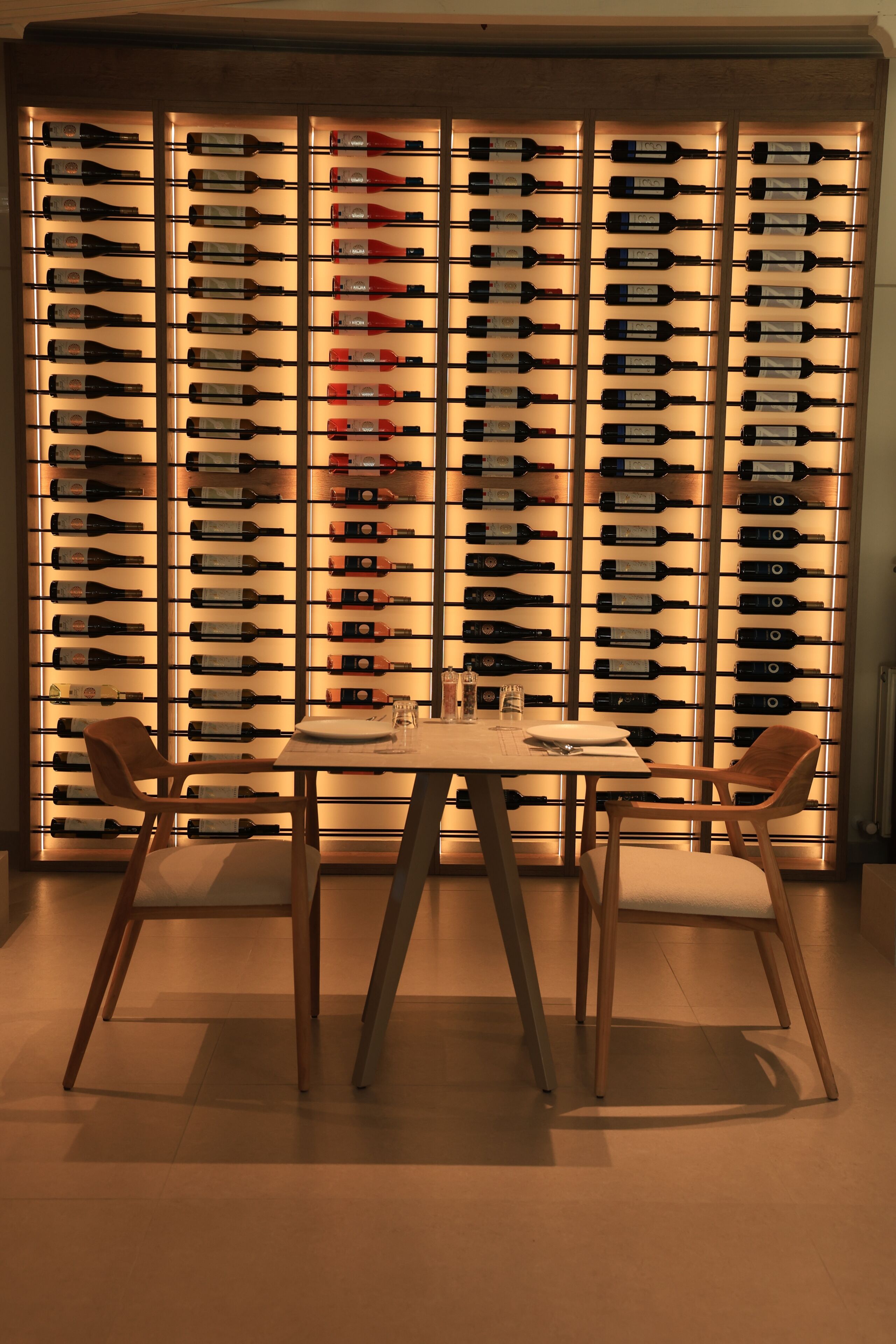 Uma área de refeições com mesa e cadeiras, uma parede com garrafas de vinho e um divisório de madeira.