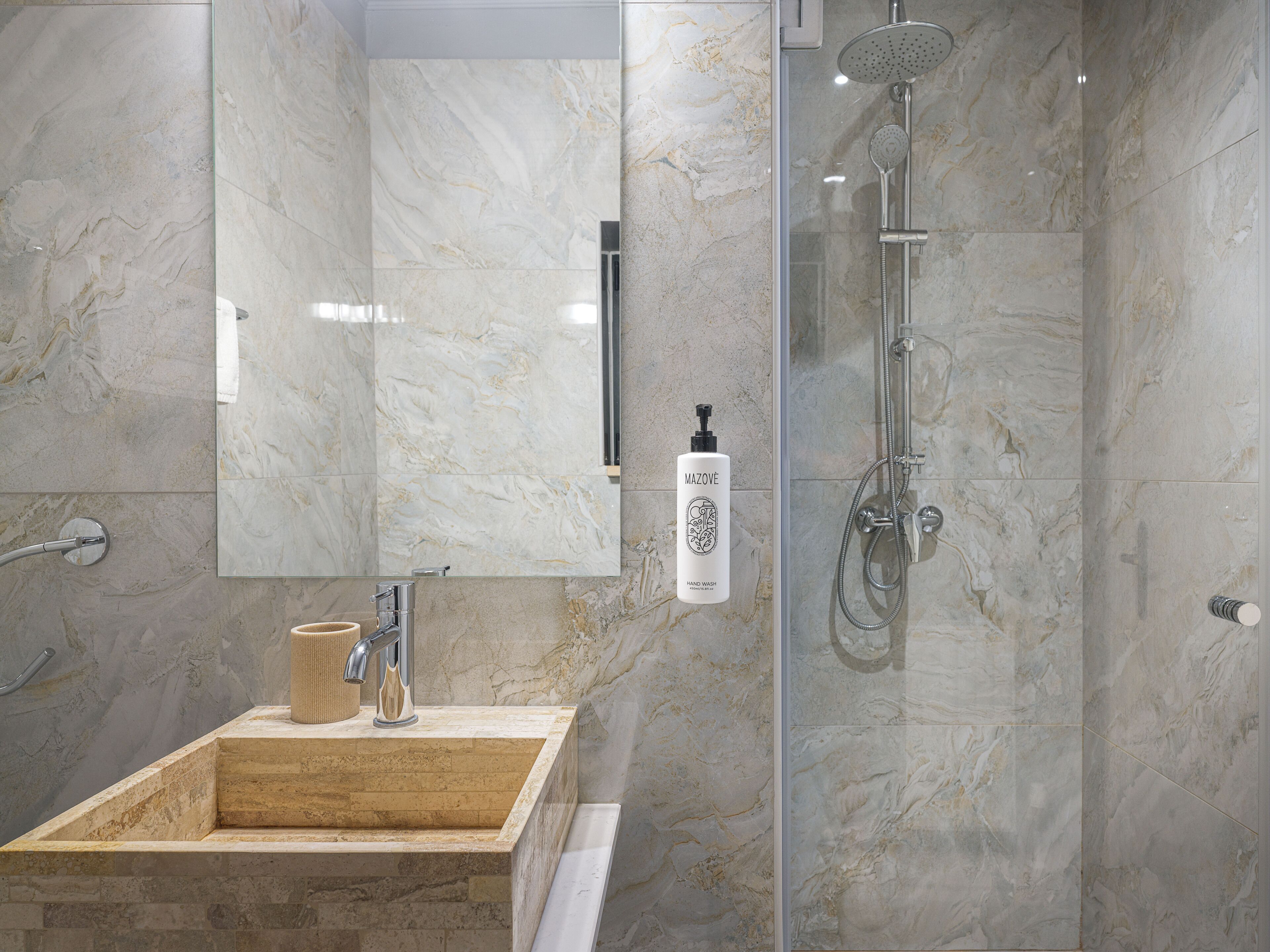 Un baño moderno con ducha de mármol, lavabo con dispensador de jabón y espejo.