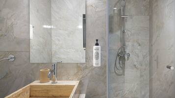 Un baño moderno con ducha de mármol, lavabo con dispensador de jabón y espejo.