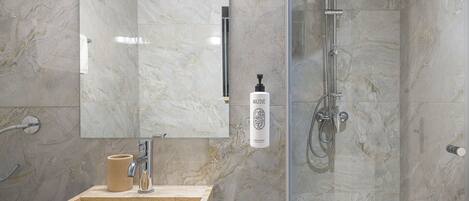 Un baño moderno con ducha de mármol, lavabo con dispensador de jabón y espejo.