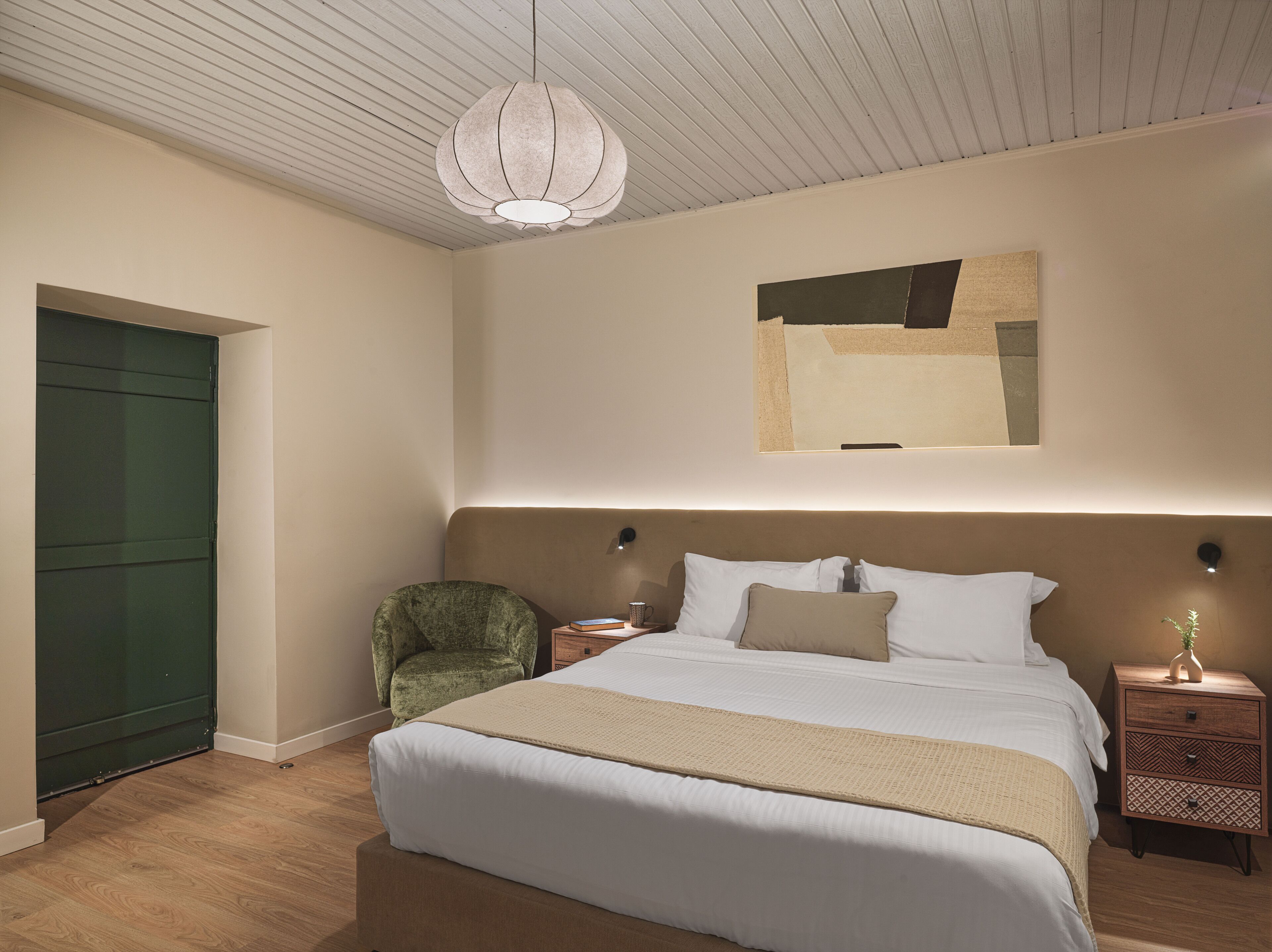 Un dormitorio con cama, una silla, una mesita de noche y una obra de arte en la pared.