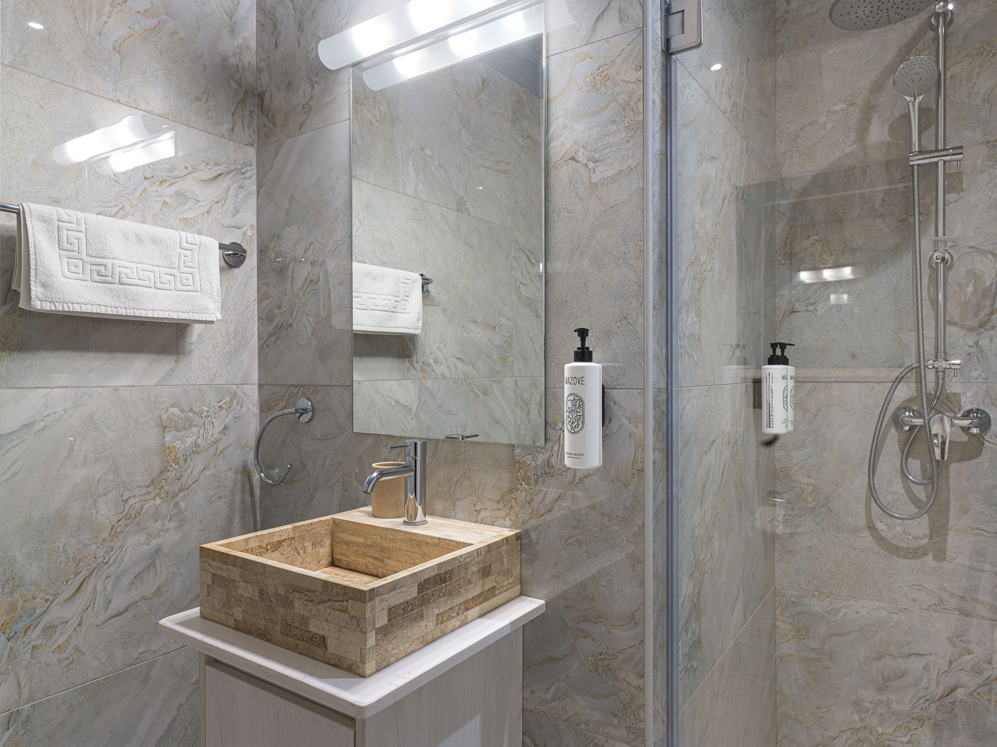 Un baño con pared de mármol, lavamanos de madera, cabina de ducha de vidrio y un espejo con toallero.