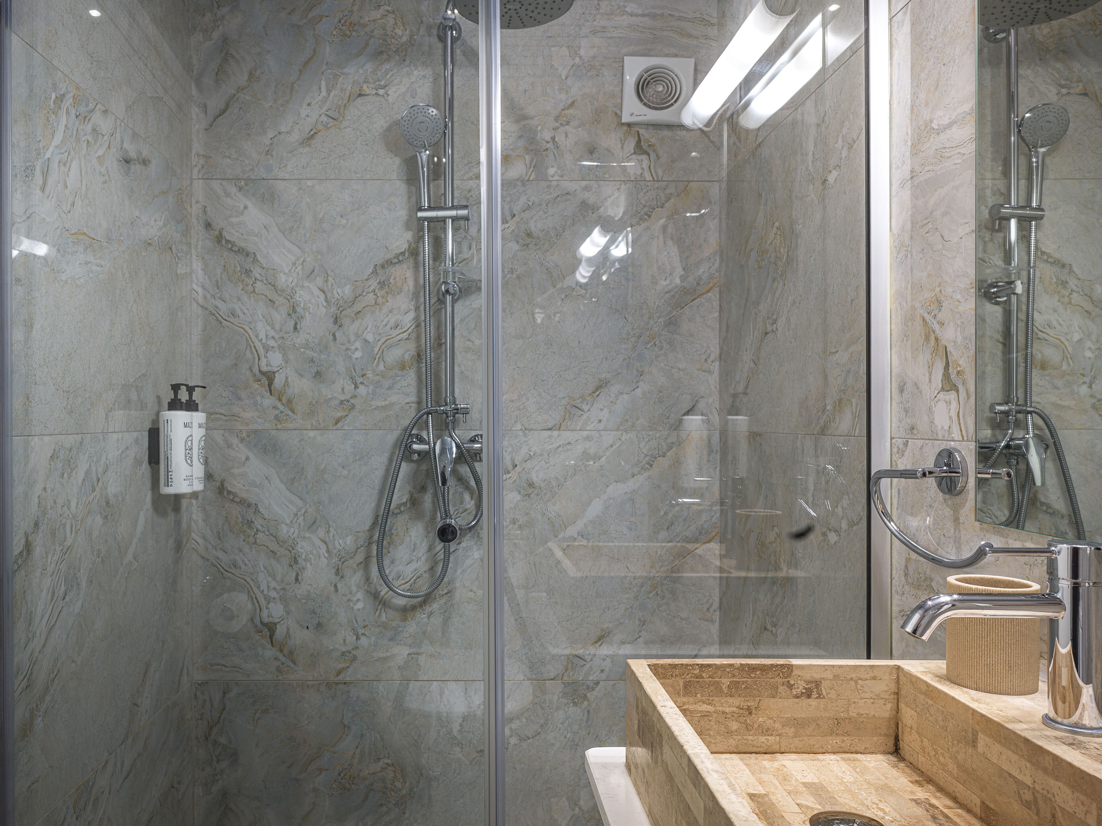Un baño moderno con ducha envuelta en vidrio, paredes de mármol y tocador de madera con lavamanos.