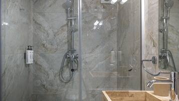 Un baño moderno con ducha envuelta en vidrio, paredes de mármol y tocador de madera con lavamanos.
