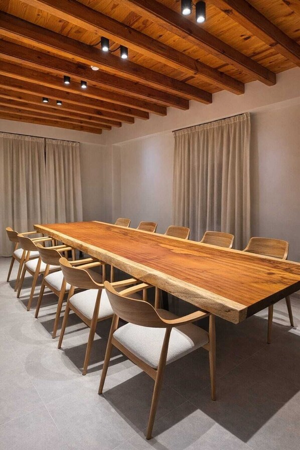 A conference room with a long wooden table, six chairs, and a high wooden ceiling with exposed beams and recessed lighting.