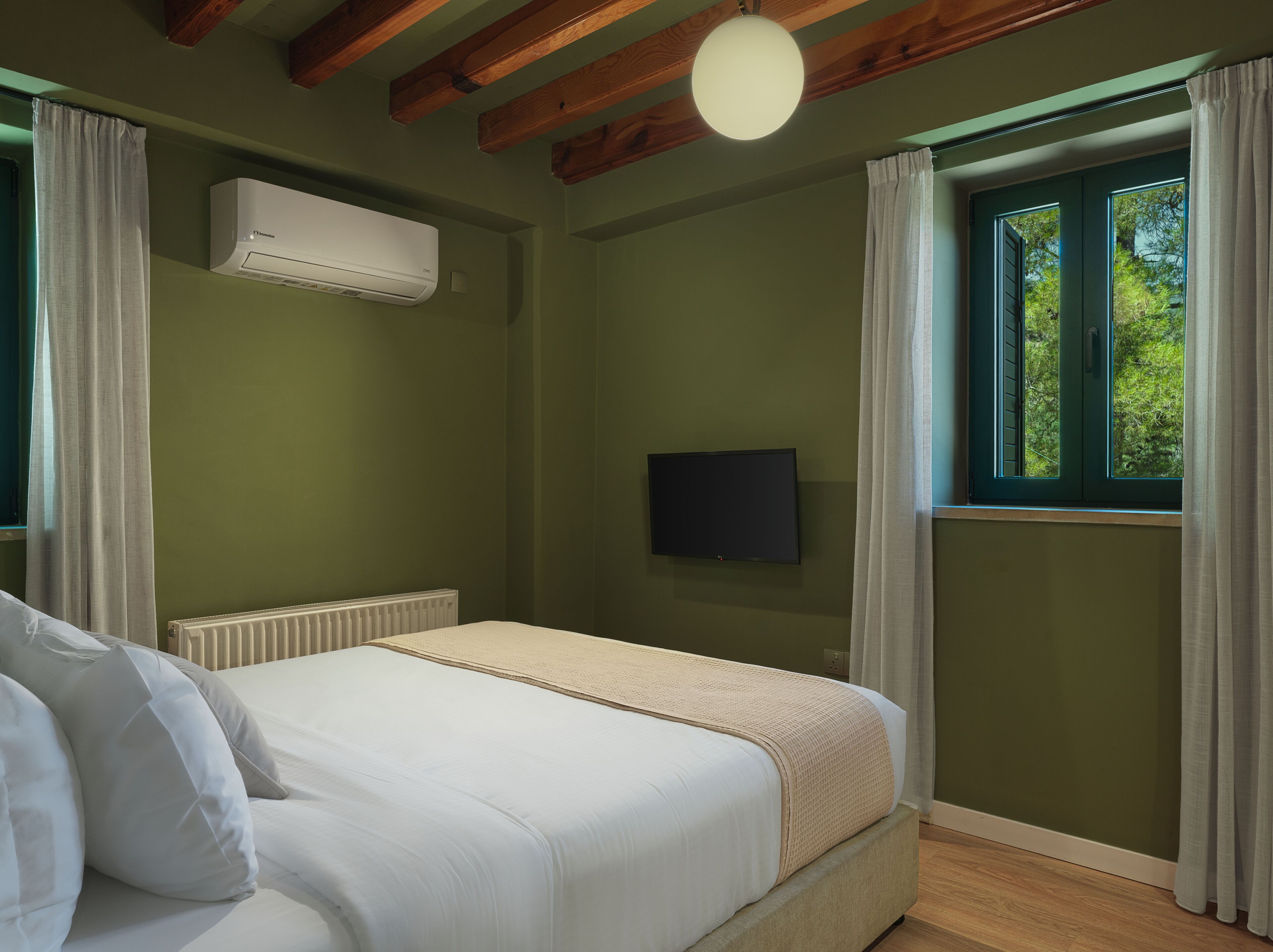 A bedroom with a bed, an air conditioning unit, a television, and a window with curtains.
