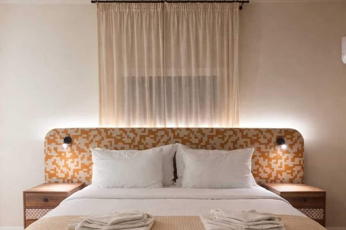 A neatly made bed with pillows, a headboard with a pixelated pattern, and a bedside table with a lamp.