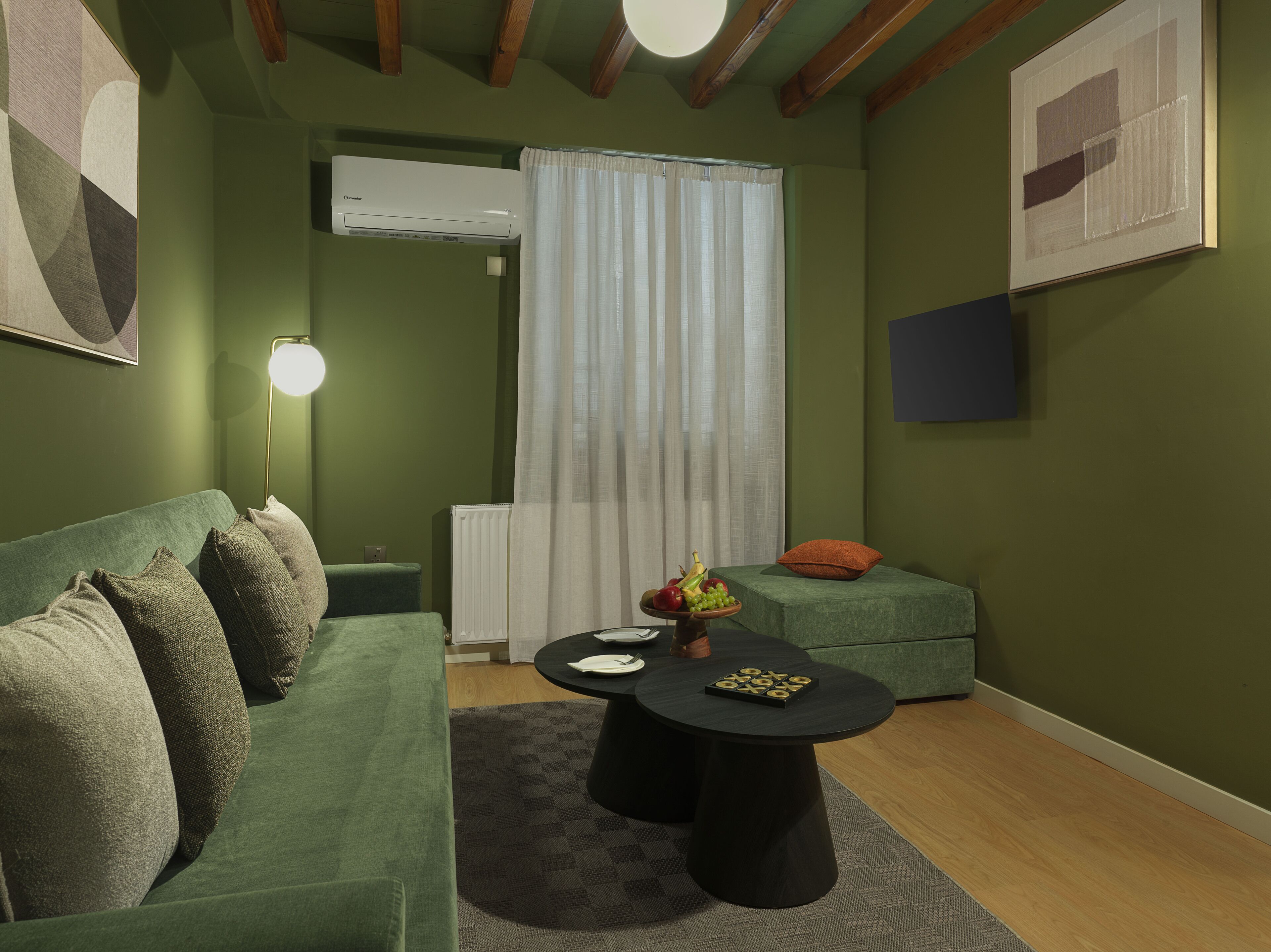 A cozy room with a green sofa, a round table with fruits, a lamp, and a radiator.