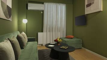 A cozy room with a green sofa, a round table with fruits, a lamp, and a radiator.