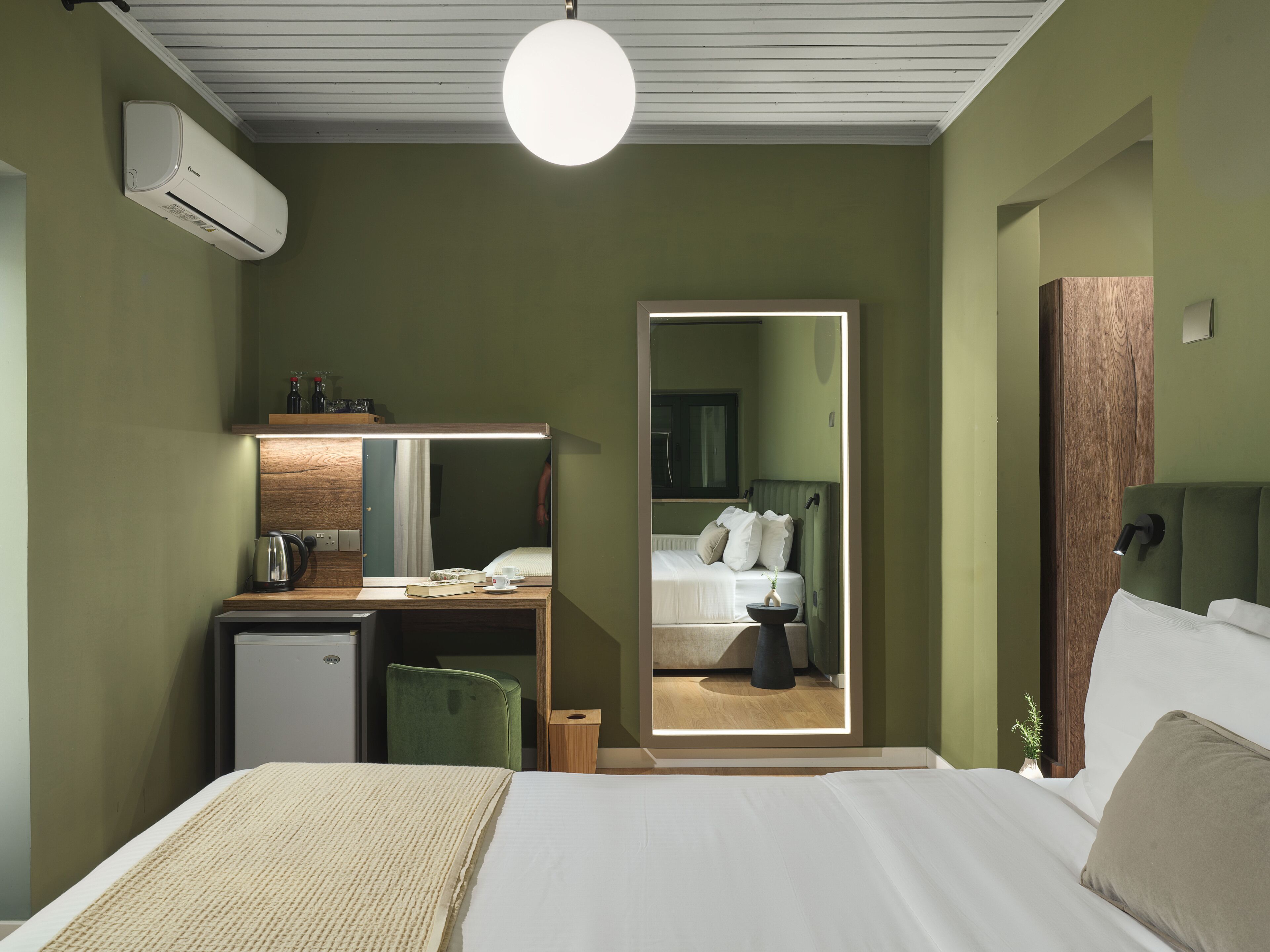 Hotellihuone, jossa on sänky, työpöytä tietokoneella, peili ja ikkuna.