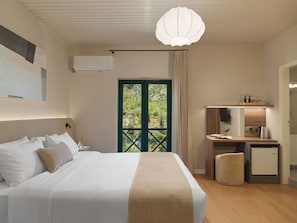 A bedroom with a bed, a desk, a small kitchenette, and a view through a door.