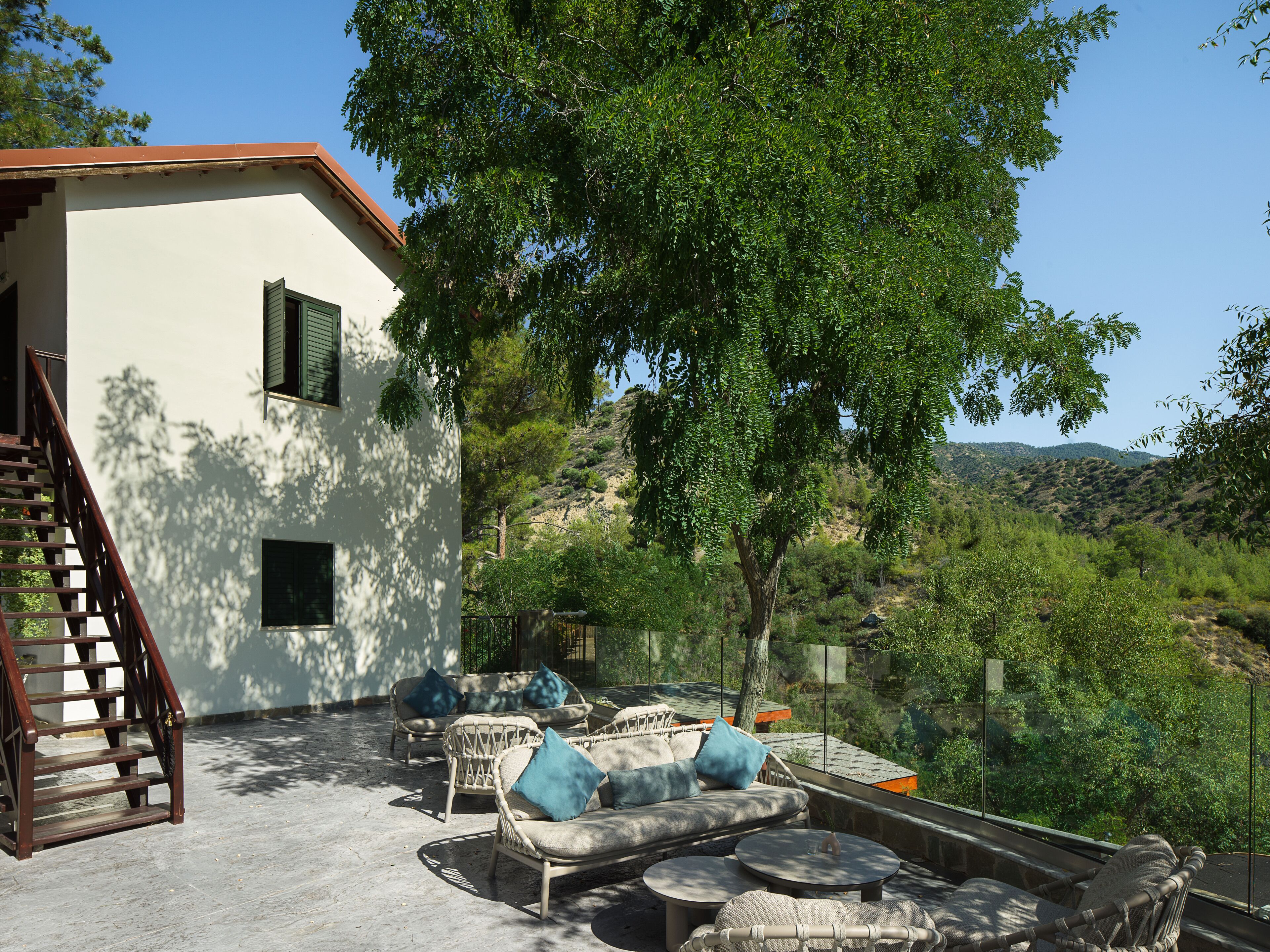 A modern outdoor seating area with wicker furniture and a stone floor, overlooking a hillside.