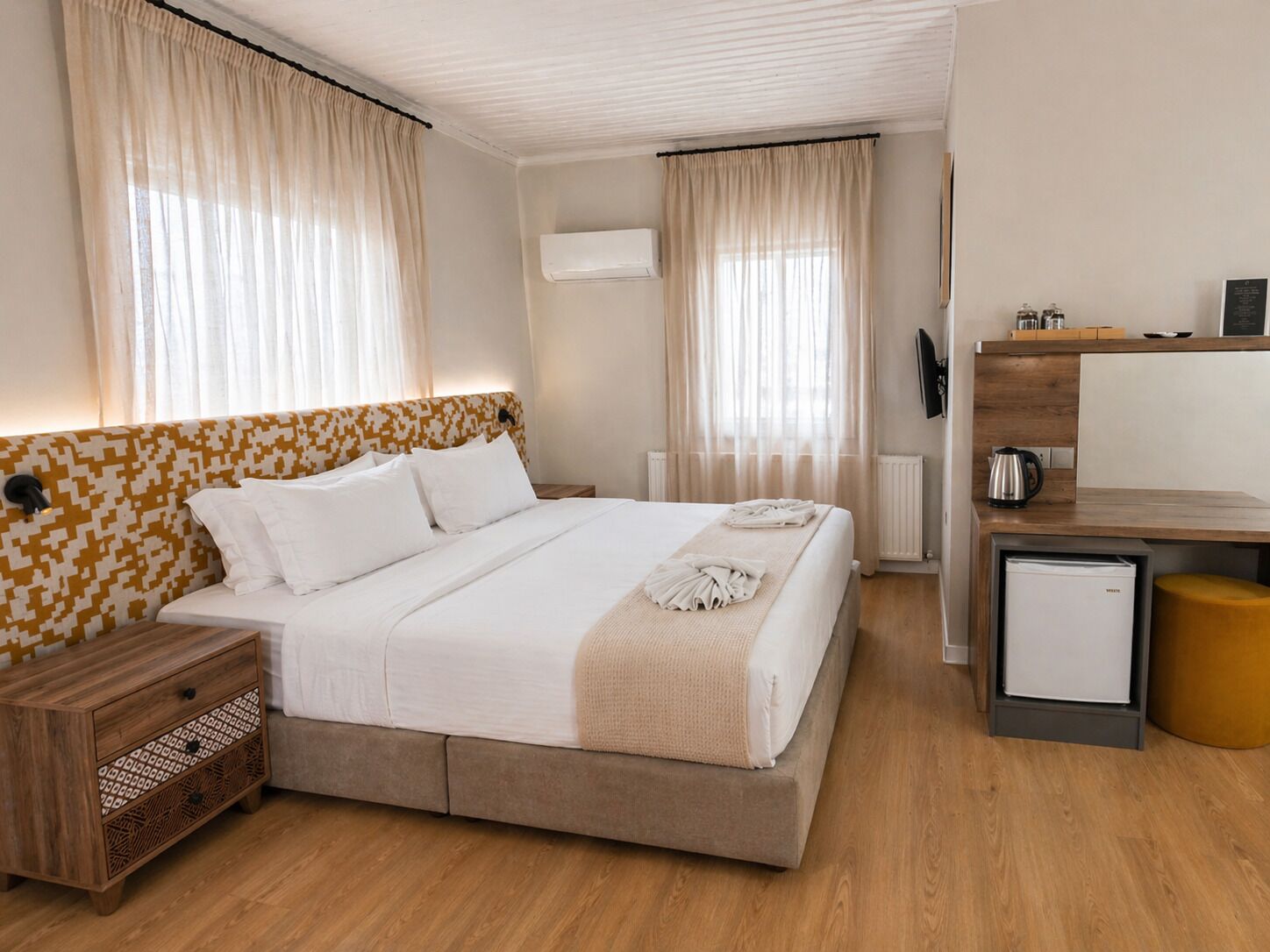 A hotel room with a bed, bedside table, wardrobe, desk, and a small kitchenette.