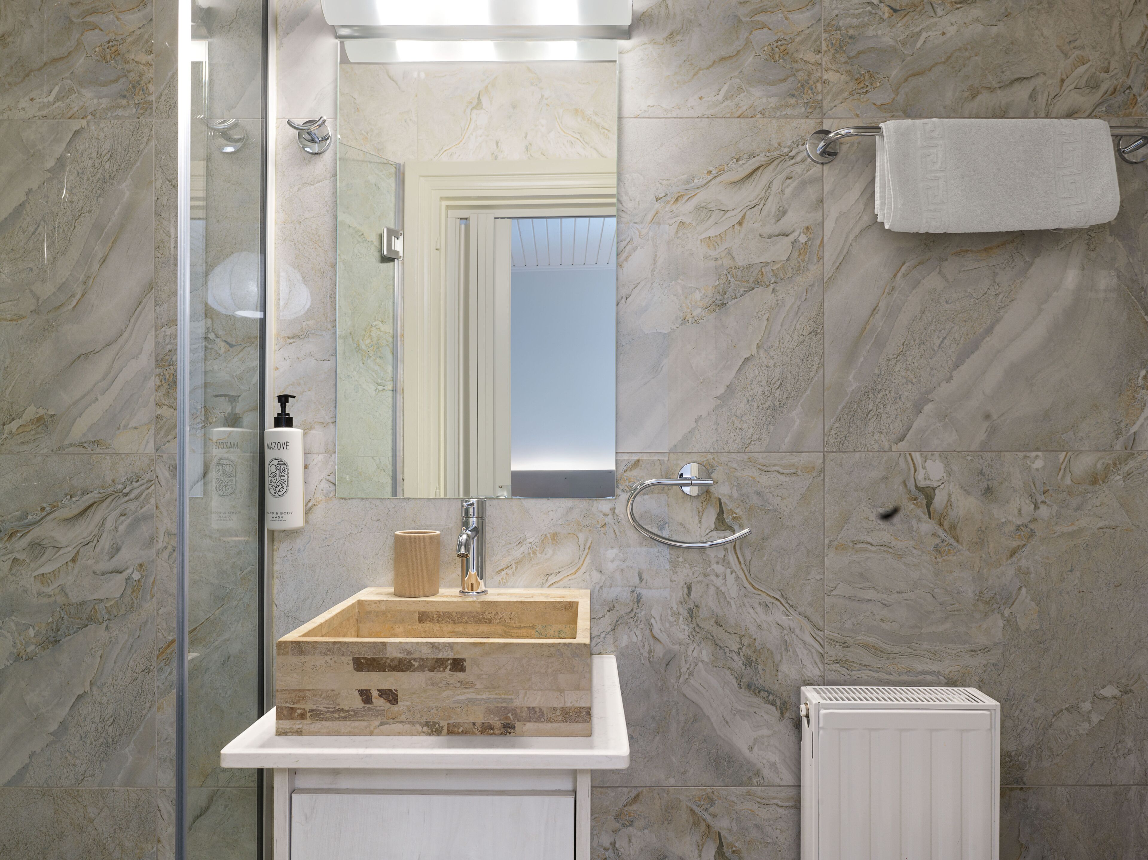 Un baño con pared de mármol, un lavamanos blanco, un perchero para toallas y una cabina de ducha de vidrio.