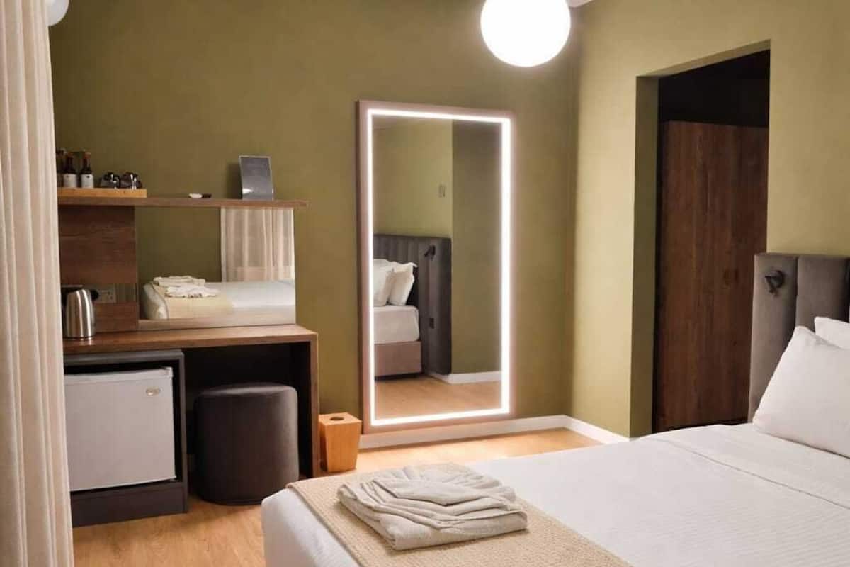 A hotel room with a bed, bedside table, mirror, and a small desk with a chair.
