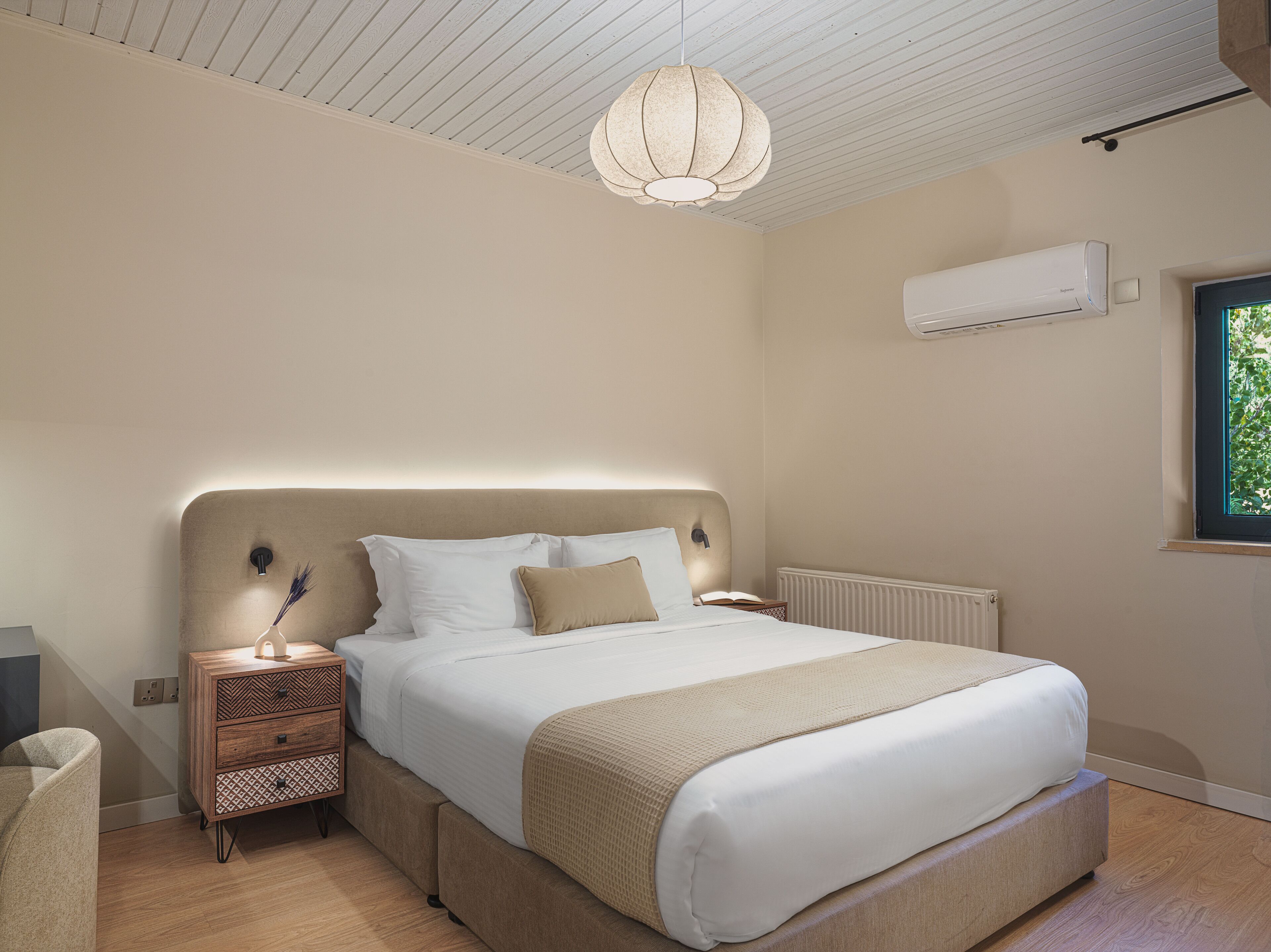Un dormitorio con cama, mesitas de noche, lámpara colgante, equipo de aire acondicionado y ventana.