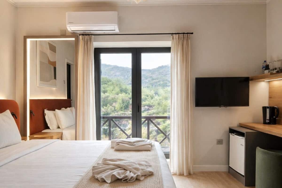 A hotel room with a bed, a desk, a TV, and a balcony with a view.