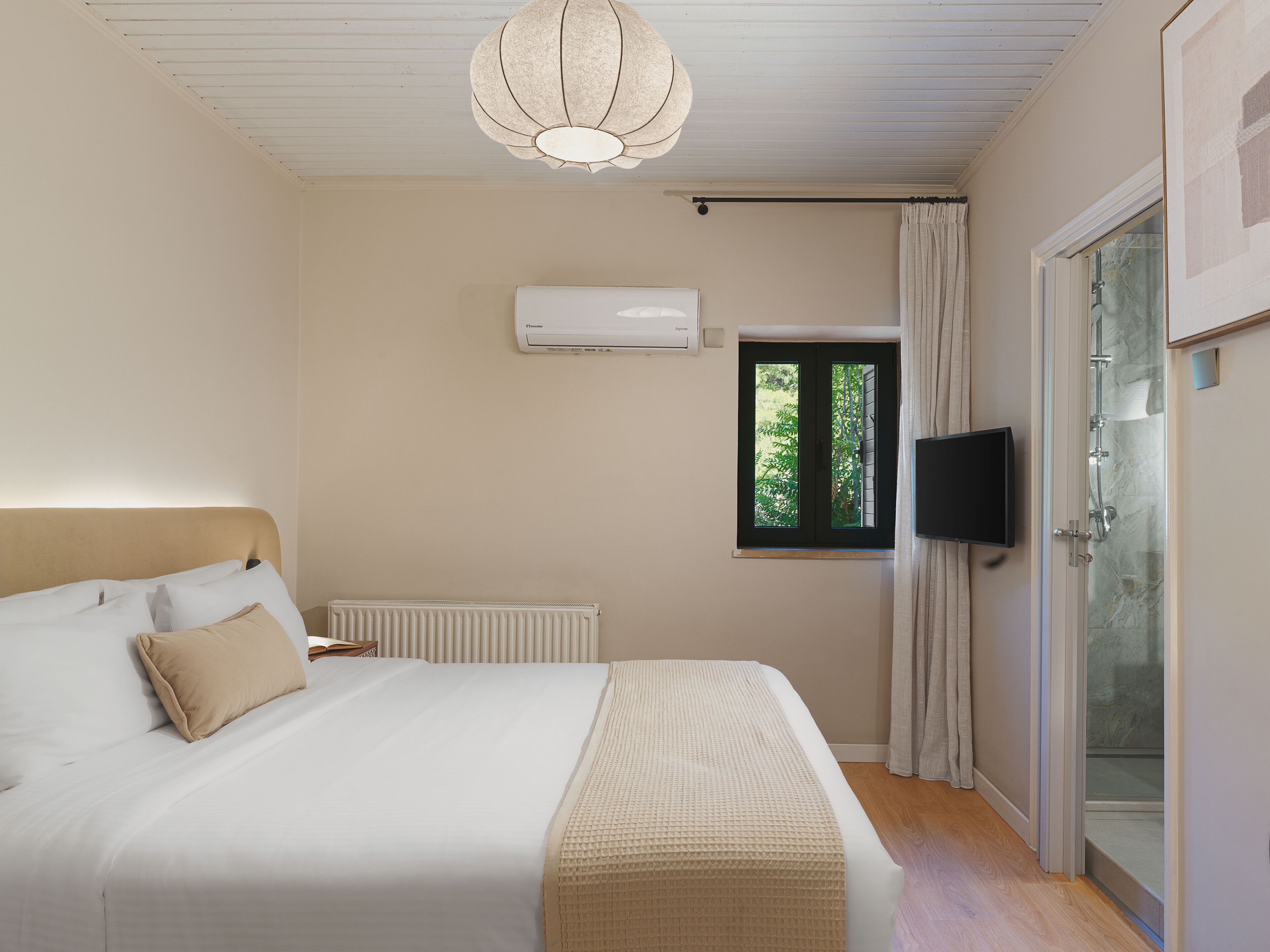 A bedroom with a bed, an air conditioning unit, a window with curtains, and a television.