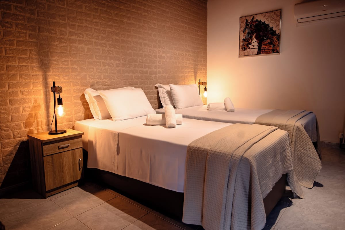 A hotel room with two beds, a nightstand, a wall-mounted air conditioner, and a painting.