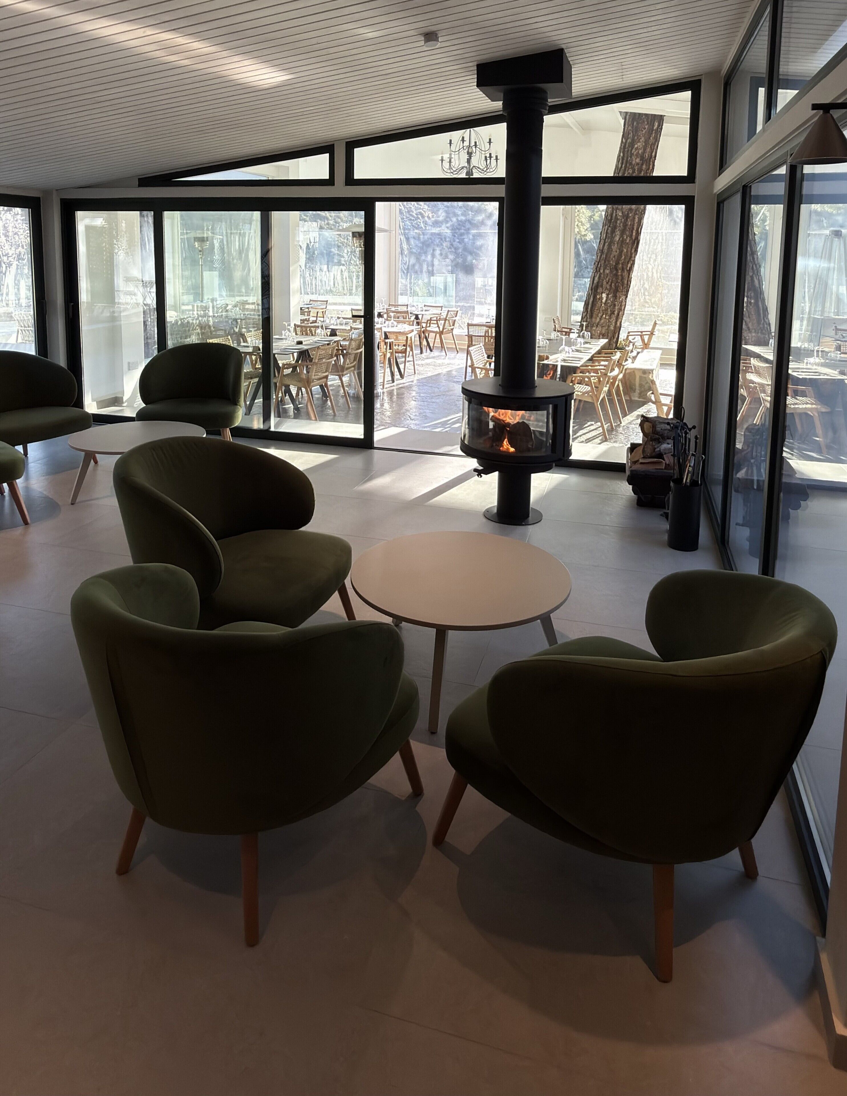 A modern interior with a central fireplace, round tables, and green chairs.