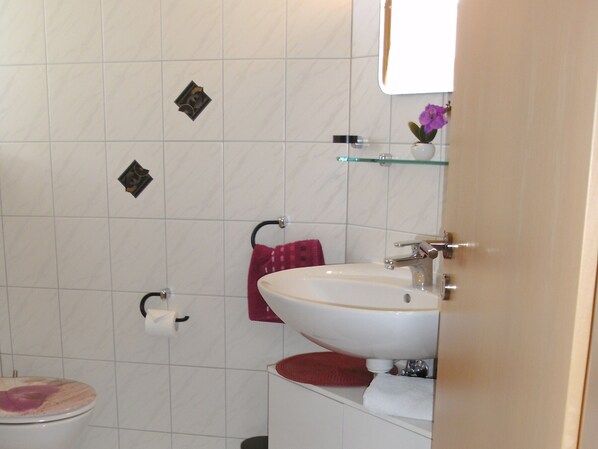 A bathroom with a toilet, sink, and a glass shelf.