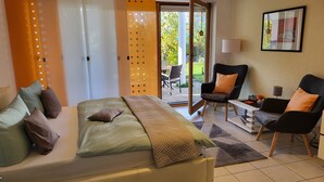 Ein modernes Hotelzimmer mit einem Bett, zwei Sesseln, einem kleinen Tisch und Blick ins Freie.