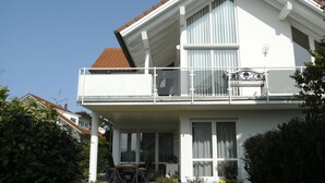 Ein zweistöckiges Gebäude mit Balkon, großen Fenstern und einem Ziegeldach.