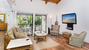Amplia sala de estar con techo de madera, un sofá, una mesa de centro, un televisor montado en la pared y un balcón con vistas a zonas verdes.