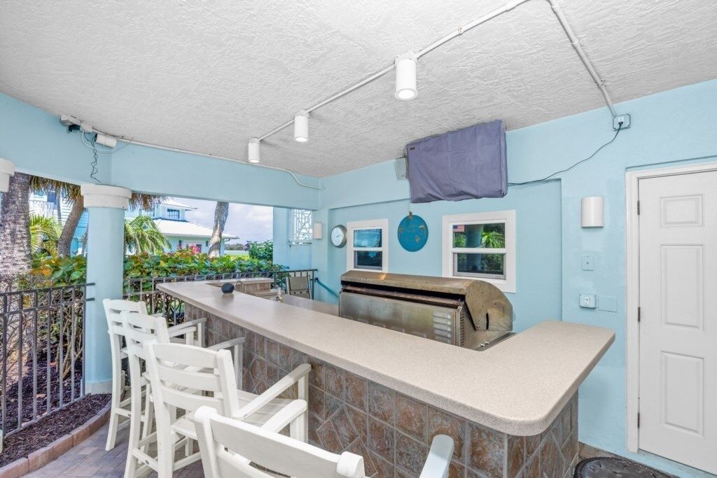 An outdoor bar area with a counter, white chairs, and a grill.