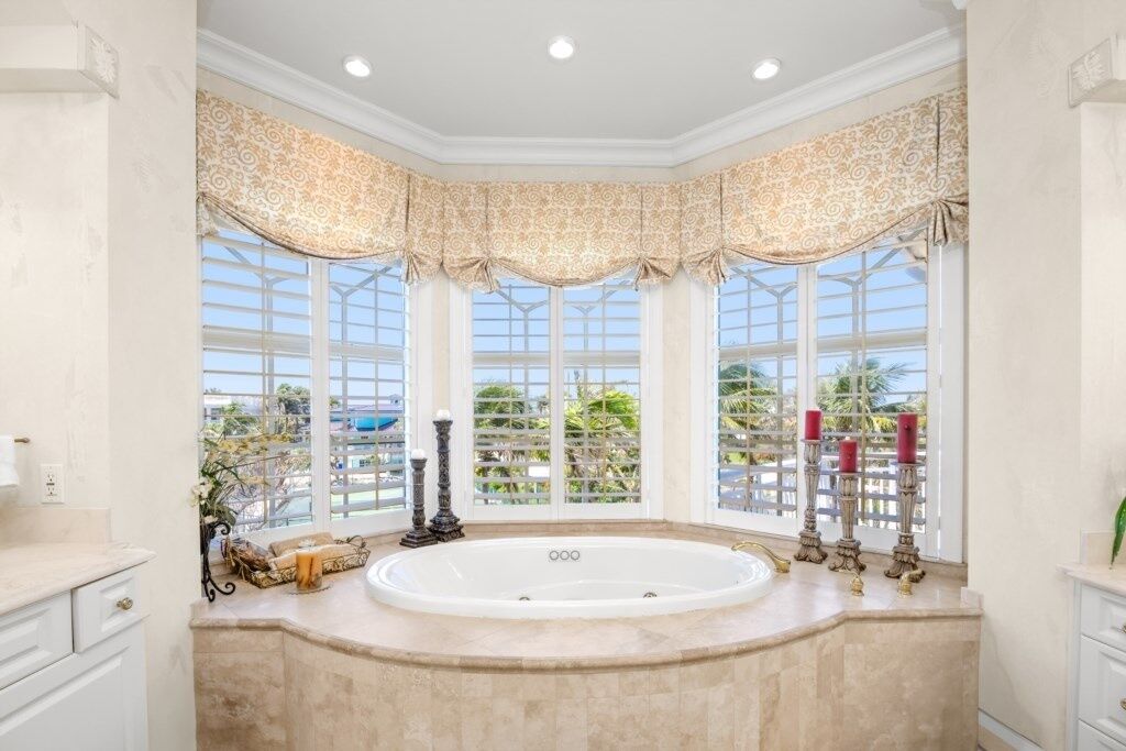 A luxurious bathroom with a large bathtub, ornate window valances, and a view of the outdoors.