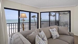Una habitación con vistas a la playa, un sofá con cojines estampados y una lámpara.