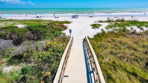 Un paseo marítimo de madera que conduce a una playa con cielos despejados y aguas tranquilas.