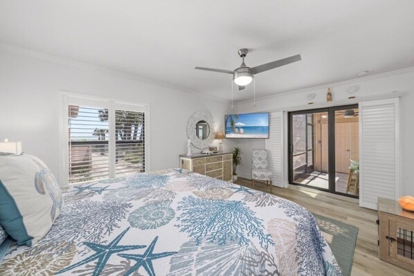 A bedroom with a bed, a ceiling fan, a TV, a sliding glass door, and a view of the outdoors. - Coquina Beach 2c 2 Bedroom Condo (Sanibel)