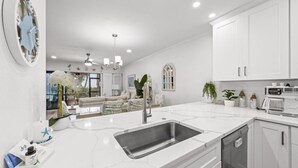 Una cocina moderna con armarios blancos, un lavamanos grande y una zona de comedor al fondo.