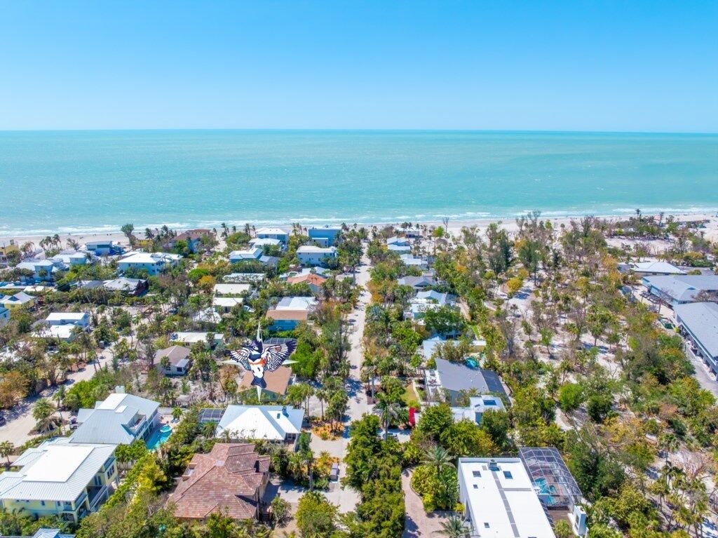 An aerial view of a coastal residential area with houses, some with visible swimming pools, and a clear view of the ocean.