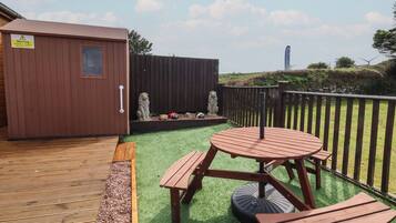 A wooden deck with a picnic table and benches, a small shed, and two stone lion statues.