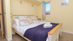 A neatly made bed with a blue quilt, white pillows, and a rolled towel on the side.