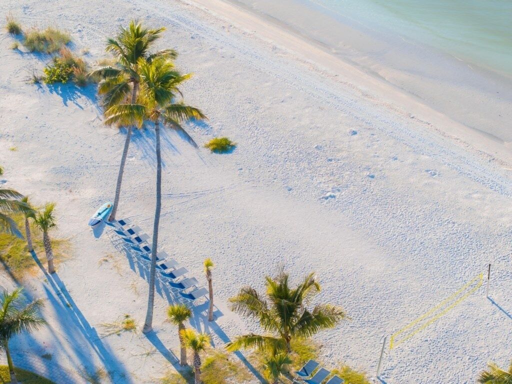 Ein Luftbild eines Strandes mit Palmen, Liegestühlen und einem Boot.